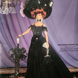 May include: A doll in a black crochet costume, including a wide-brimmed hat, long dress, and beaded purse. The costume is from the "Crochet Collection Costume Volume 76". The doll is holding a black parasol. The text on the image reads "1898 Parisian Merry Widow".
