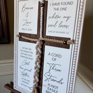 May include: A framed wedding sign with a white and brown cross design. The sign includes the names "Bianca & Zane" and the date "May 31, 2025". It features inspirational quotes and Bible verses about love and marriage.
