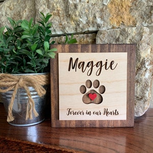 May include: Wooden sign with the name Maggie and a paw print with a red heart in the center. The sign reads "Forever in our Hearts".