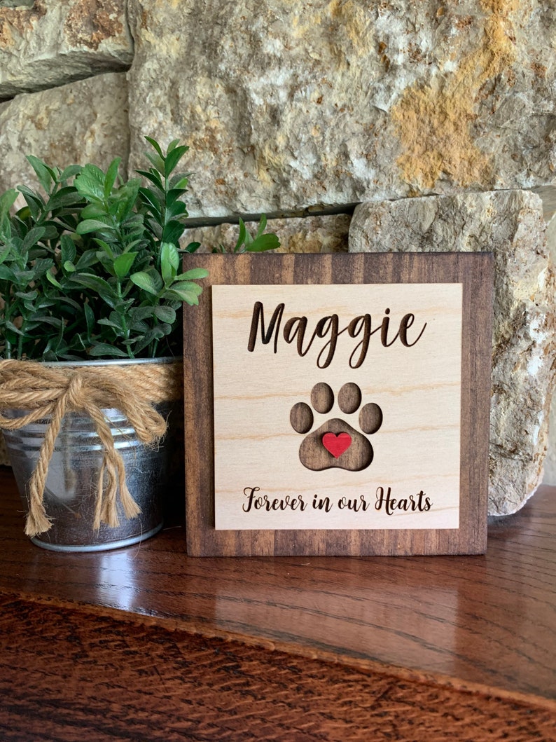 May include: Wooden sign with the name Maggie and a paw print with a red heart in the center. The sign reads "Forever in our Hearts".