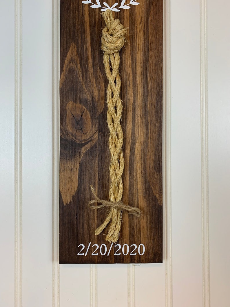 May include: A wooden sign with a white heart design and a rope tied in a knot. The date 2/20/2020 is written on the sign.