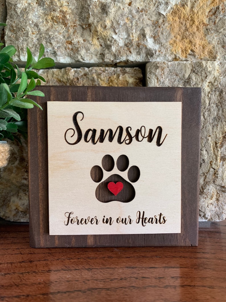 May include: Wooden sign with a paw print cutout and a red heart in the center. The sign reads "Samson Forever in our Hearts".