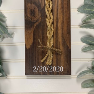 May include: A wooden sign with a braided rope tied in a bow and the date 2/20/2020 written in white paint.