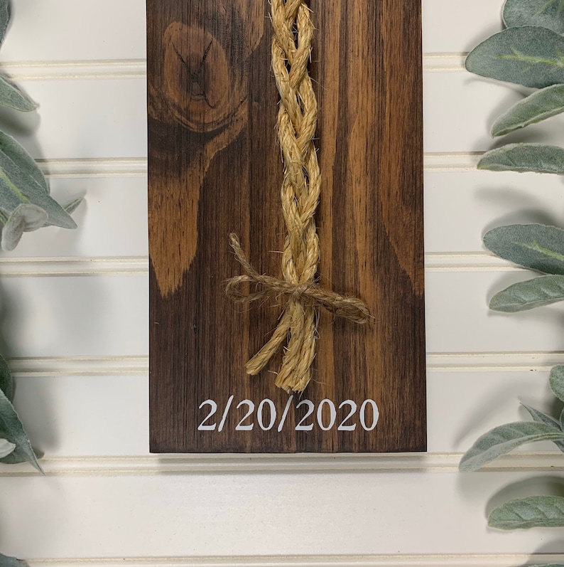 May include: A wooden sign with a braided rope tied in a bow and the date 2/20/2020 written in white paint.