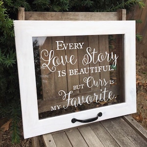 May include: White wooden frame with a glass pane and a black metal handle. The glass pane has a white vinyl decal with the text "Every love story is beautiful, but ours is my favorite."