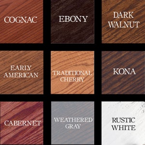 May include: Nine wood stain samples are displayed, each with a different colour name. The colours are Cognac, Ebony, Dark Walnut, Early American, Traditional Cherry, Kona, Cabernet, Weathered Grey, and Rustic White.