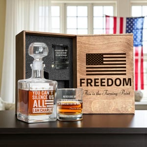 Pode incluir: Um conjunto de presente de madeira com um jarro, dois copos e uma caixa de madeira. O jarro e um copo têm texto gravado. A caixa tem um desenho da bandeira americana e a palavra "FREEDOM". O conjunto é exibido em uma superfície escura.