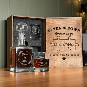 May include: A wooden gift set with a decanter, two glasses, and a shot glass. The decanter and glasses are engraved with names and a date. The wooden box is engraved with "40 Years Down" and "I love you to pieces".