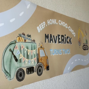 May include: A brown paper banner with a cartoon illustration of a garbage truck filled with gifts. Text includes "Beep, Honk, Choo-Choo", "Maverick Turns Two!" and "Happy Birthday" on a banner. The banner also features a road and a construction vehicle.