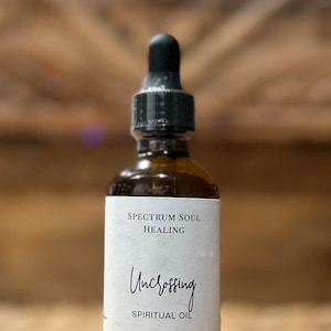 May include: A brown glass bottle with a black dropper, labeled "Spectrum Soul Healing" and "Uncrossing Spiritual Oil." The label also indicates a 2 oz / 50ml volume. The background is a woven texture.