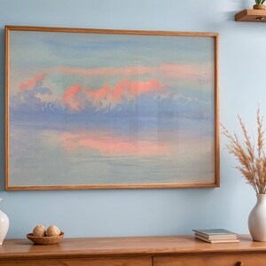 May include: A framed watercolor painting of a sunset with pink and orange clouds over a blue and purple sky. The artwork is in a light brown wooden frame. The painting hangs above a wooden cabinet with decorative items.