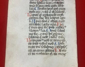 May include: A rectangular parchment manuscript page featuring dense black Latin calligraphy in a gothic script. The text is punctuated by decorative capital letters in red and blue ink, arranged in a single column on a light, textured off-white surface.