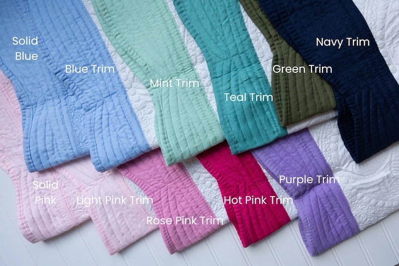 May include: A collection of quilted fabric swatches featuring white floral patterns with various coloured borders labelled Solid Blue, Blue Trim, Mint Trim, Teal Trim, Green Trim, Navy Trim, Solid Pink, Light Pink Trim, Rose Pink Trim, Hot Pink Trim, and Purple Trim.