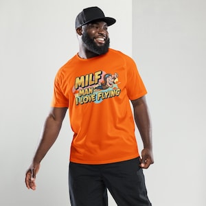 May include: Orange t-shirt with the text "MILF MAN I LOVE FLYING" and a cartoon graphic of a man flying. The shirt is short-sleeved and worn with a black baseball cap and black pants.