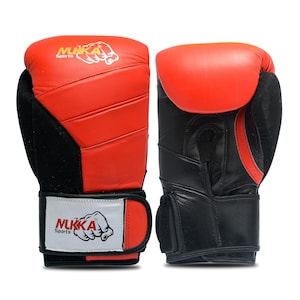 Puede incluir: Un par de guantes de boxeo rojos y negros. La parte superior de los guantes es roja, mientras que la palma y la muñeca son negras. El nombre de la marca "NUKKA Sports" está impreso en las correas blancas. Para boxeo u otros deportes de combate.