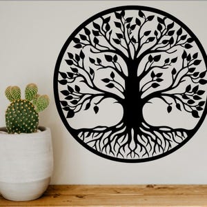 May include: Black metal tree of life wall art. The tree is enclosed in a circular frame, with detailed branches, leaves, and roots. A potted cactus sits on a wooden surface to the left of the wall art.