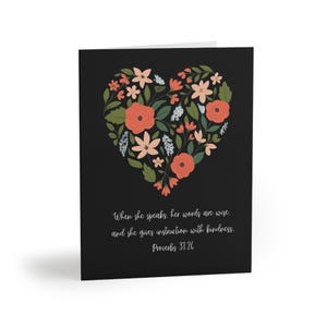 Puede incluir: Una tarjeta de felicitación negra con un diseño de corazón floral en tonos melocotón, coral y verde. La tarjeta incluye el texto "Cuando habla, sus palabras son sabias, y da instrucción con bondad. Proverbios 31:26."