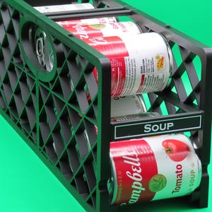 Può includere: Organizzatore di lattine in plastica nera che contiene diverse lattine di zuppa Campbell's. Le lattine sono rosse e bianche con il logo Campbell's e grafica di pomodori. L'organizzatore ha un design a forma di diamante e l'etichetta "SOUP".