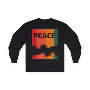 Puede incluir: Camiseta negra de manga larga con un diseño gráfico. El diseño presenta la palabra "PEACE" en letras negras en bloque sobre un patrón de rayas verticales coloridas y desgastadas en rojo, naranja y verde azulado.