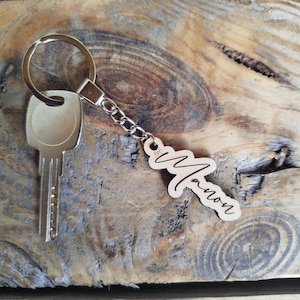 Peut inclure: Une clé et un porte-clés en bois avec le nom "Manon". Le porte-clés est attaché à un anneau et une chaîne en métal. La clé est de couleur argent.