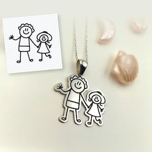 Op de afbeelding: Een zilveren hangerketting met een gestileerd familieontwerp. De hanger toont een ouder en kind die elkaars hand vasthouden, in een eenvoudige, omtrekachtige illustratiestijl. De ketting wordt gepresenteerd op een licht oppervlak, met de tekst "THE LITTLE ARTIST" bovenaan.