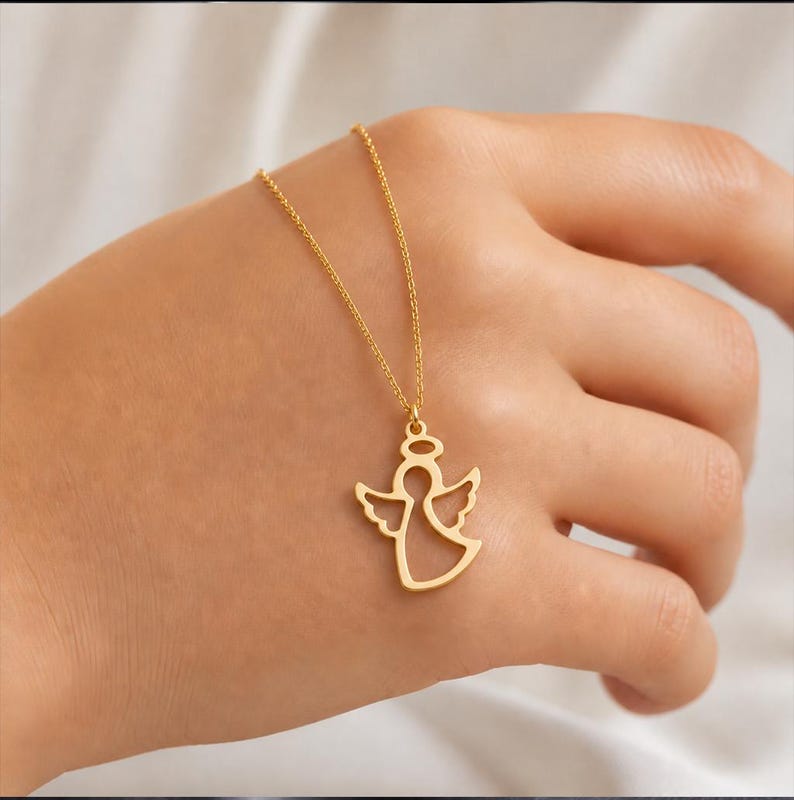 K&ouml;nnte beinhalten: Eine goldfarbene Engels-Anh&auml;nger-Halskette. Der Anh&auml;nger ist ein Ausschnitt eines Engels mit Heiligenschein und Fl&uuml;geln. Die Halskette wird auf einer Hand pr&auml;sentiert.