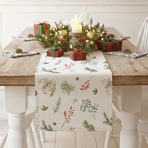 Peut inclure: Une table de salle à manger en bois décorée pour un repas de Noël. Elle est ornée d'un chemin de table blanc avec un imprimé botanique, de boîtes cadeaux rouges et d'un centre de table avec des bougies. Des chaises blanches entourent la table.