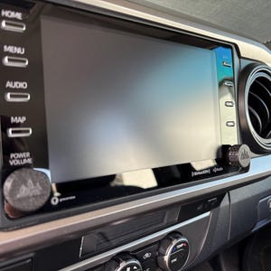 May include: A car's dashboard featuring a large, rectangular infotainment screen. The screen is surrounded by buttons labeled "HOME", "MENU", "AUDIO", "MAP", and "POWER VOLUME". A silver trim frames the screen and air vents.