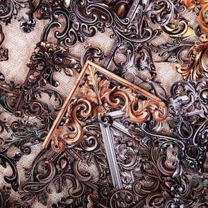 Puede incluir: Una colección de soportes de esquina decorativos de metal ornamentados, en acabados dorados y plateados. Los soportes presentan intrincados trabajos de desplazamiento y diseños florales.