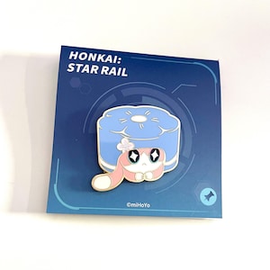 May include: A pin featuring a cartoon character with a blue and white design, with a pink and white character in front of a blue object. The pin is on a blue card with the text "HONKAI: STAR RAIL". The copyright reads "&copy;miHoYo".