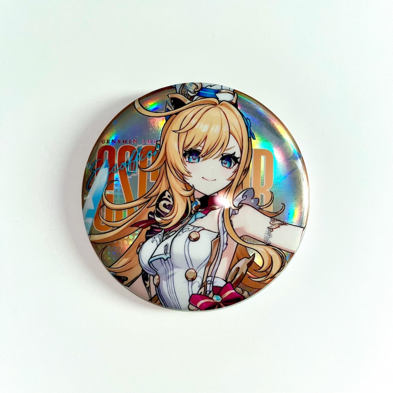 Pu&ograve; includere: Un bottone rotondo e olografico con un personaggio anime sorridente con capelli biondi e occhi blu. Il personaggio indossa un abito bianco con dettagli rossi. Il bottone presenta il testo "GENSHIN IMPACT" e il nome del personaggio.