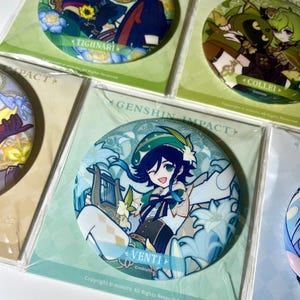 May include: A collection of round character badges from the Genshin Impact series. Each badge features a different character illustration with their name. The badges are packaged in clear plastic and have a glossy finish.