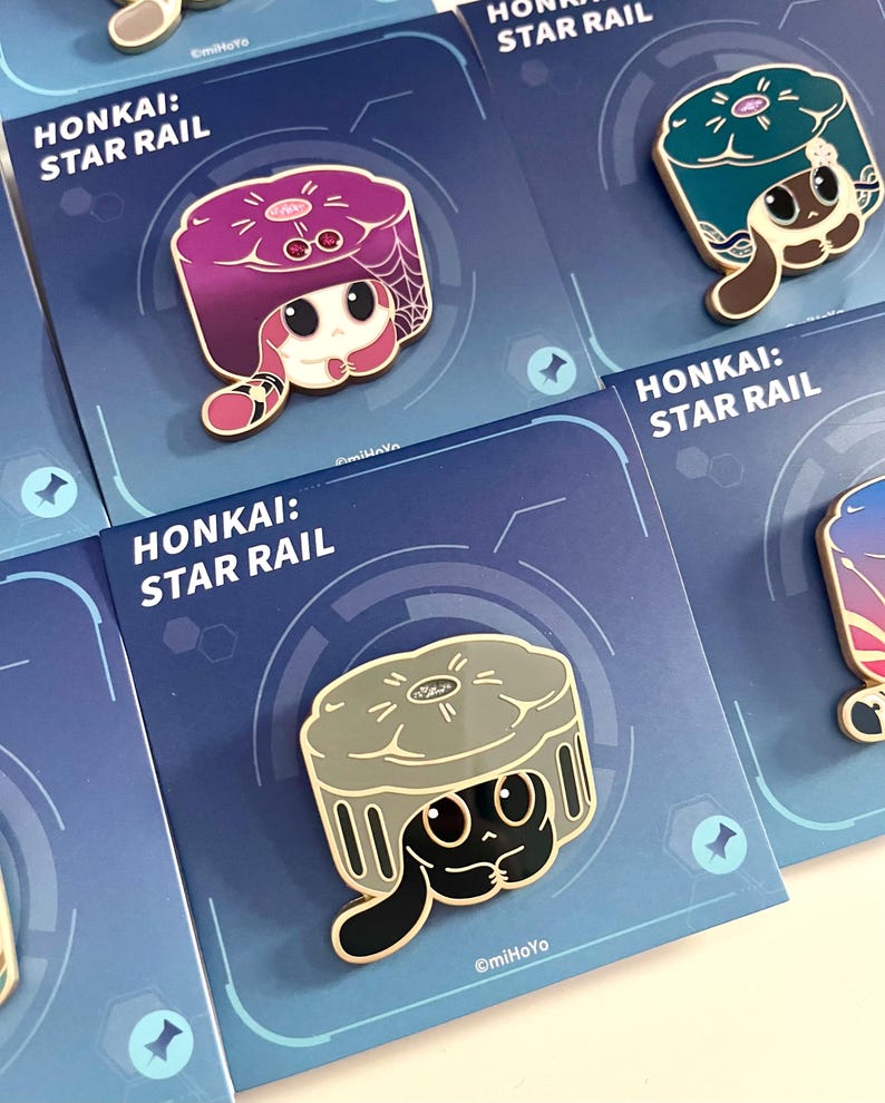 May include: Enamel pins featuring characters from "Honkai: Star Rail." The pins showcase various characters with unique designs and colors, set against a blue background with the game's logo. Each pin is attached to a card.