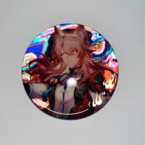 May include: A round, iridescent button featuring a character with pink hair and fox ears. The character is wearing a red and gold outfit with a blue sash. The background is a swirling pattern of blue, green, and red.