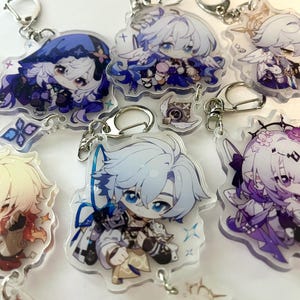 K&ouml;nnte beinhalten: Sammlung von Schl&uuml;sselanh&auml;ngern mit Anime-Charakteren. Jeder Schl&uuml;sselanh&auml;nger zeigt ein anderes Charakterdesign mit leuchtenden Farben, darunter Blau, Lila und Gold. Die Schl&uuml;sselanh&auml;nger sind an silberfarbenen Metallverschl&uuml;ssen befestigt.