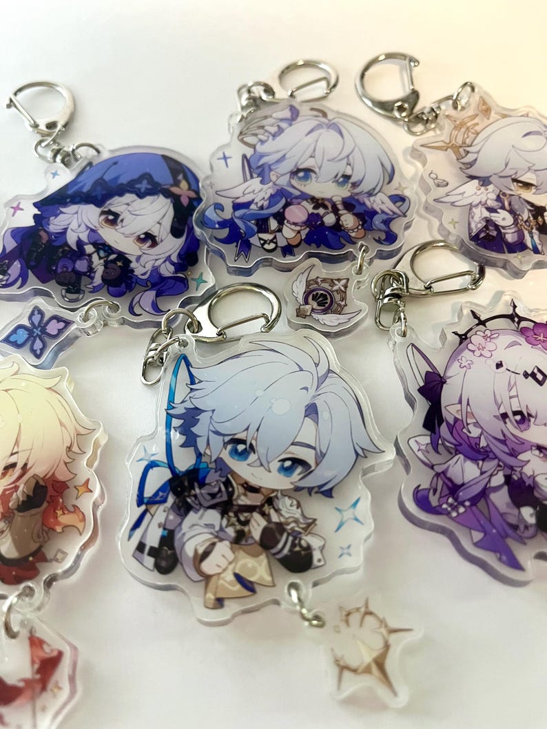 K&ouml;nnte beinhalten: Sammlung von Schl&uuml;sselanh&auml;ngern mit Anime-Charakteren. Jeder Schl&uuml;sselanh&auml;nger zeigt ein anderes Charakterdesign mit leuchtenden Farben, darunter Blau, Lila und Gold. Die Schl&uuml;sselanh&auml;nger sind an silberfarbenen Metallverschl&uuml;ssen befestigt.