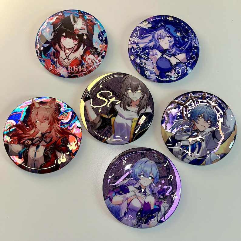 May include: Five round holographic buttons featuring anime characters. The buttons are decorated with a variety of colors and designs, including a red and black character with a fox tail, a blue and purple character with a star, a blue and purple character with a clock, a blue and purple character with a musical note, and a purple and white character with a musical note.