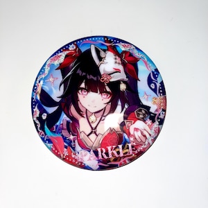 May include: A round button with a colorful anime character with long black hair and a red and white mask. The character is wearing a red and gold outfit and has pink glitter around her. The button has a pink glitter border and the word "SPARKLE" written in pink glitter.