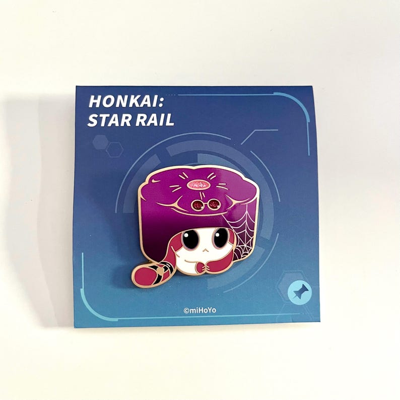 May include: A purple and white enamel pin featuring a cartoon character from Honkai: Star Rail. The character has a purple hat with a spiderweb design and a white face. The pin is on a blue card with the text "HONKAI: STAR RAIL".