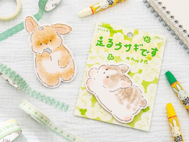 Puede incluir: Un surtido de art&iacute;culos de papeler&iacute;a con tem&aacute;tica de conejos. Incluye pegatinas de conejos, cinta decorativa y crayones. Las pegatinas tienen un estilo acuarela con tonos suaves de naranja y marr&oacute;n. El texto del embalaje est&aacute; en japon&eacute;s.