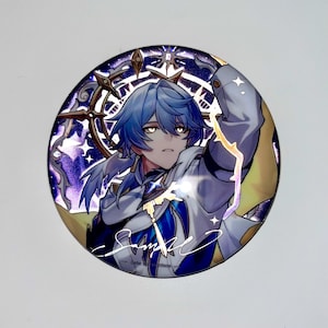 May include: A round, holographic button featuring a blue-haired anime character with a white and blue outfit. The character is surrounded by a gold and purple star-shaped design. The button has a signature at the bottom that says "Sample".
