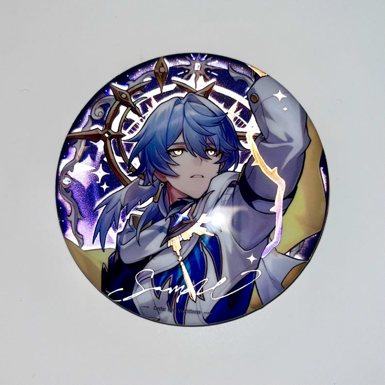 May include: A round, holographic button featuring a blue-haired anime character with a white and blue outfit. The character is surrounded by a gold and purple star-shaped design. The button has a signature at the bottom that says "Sample".