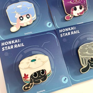 May include: Four enamel pins featuring cartoon characters from Honkai: Star Rail. Each pin has a unique design with a character wearing a hat or head covering. The pins are on blue cards with the game's name.