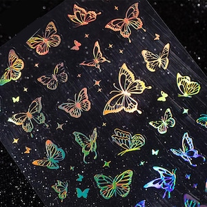 Puede incluir: Hoja de pegatinas de mariposas iridiscentes en varios tamaños y colores, incluyendo dorado, naranja, verde y azul. Las mariposas tienen patrones de alas detallados y están dispersas sobre un fondo oscuro con pequeñas estrellas.