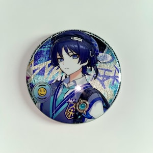 Pu&ograve; includere: Un bottone rotondo con un personaggio in stile anime con capelli e occhi blu. Il bottone ha uno sfondo blu e argento con una faccina sorridente e un logo. Il personaggio indossa un'uniforme blu e bianca.
