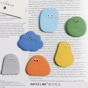 May include: A collection of colorful, die-cut sticky notes in various shapes, including a cloud, a ghost, and a blob, each with a simple, expressive face. The notes are in shades of blue, orange, yellow, and green.