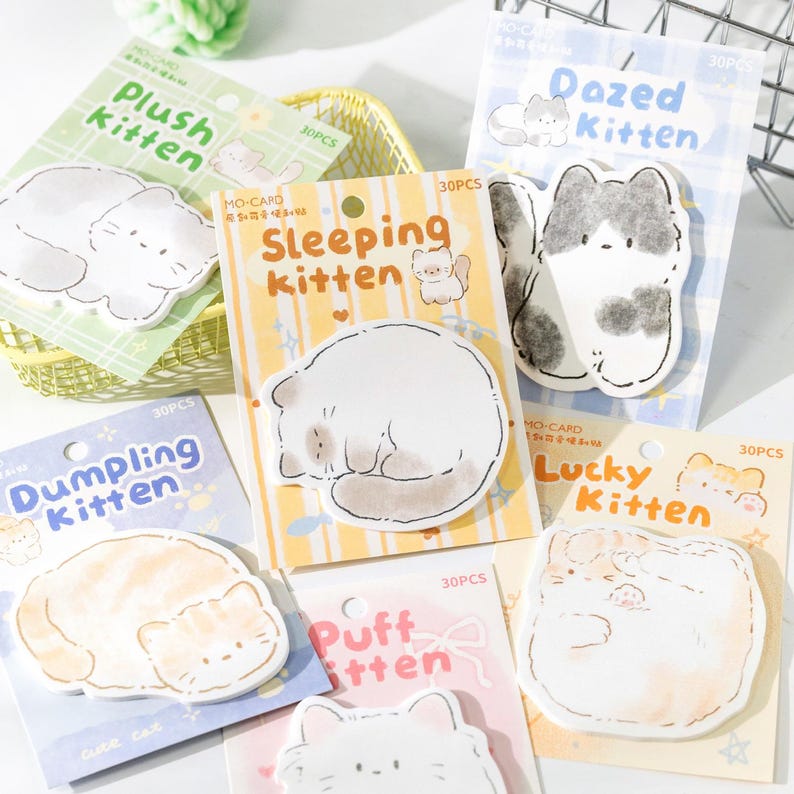 Puede incluir: Un conjunto de notas adhesivas con forma de gato, con ilustraciones y frases como "Dazed Kitten" y "Lucky Kitten". Cada paquete contiene 30 notas adhesivas.