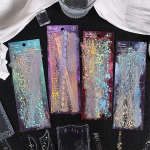 May include: Four sheets of clear, iridescent, decorative stickers with various designs. The stickers feature a variety of patterns, including musical notes, flowers, and geometric shapes. The stickers are packaged in clear plastic sleeves and labeled with the number 30 pieces.