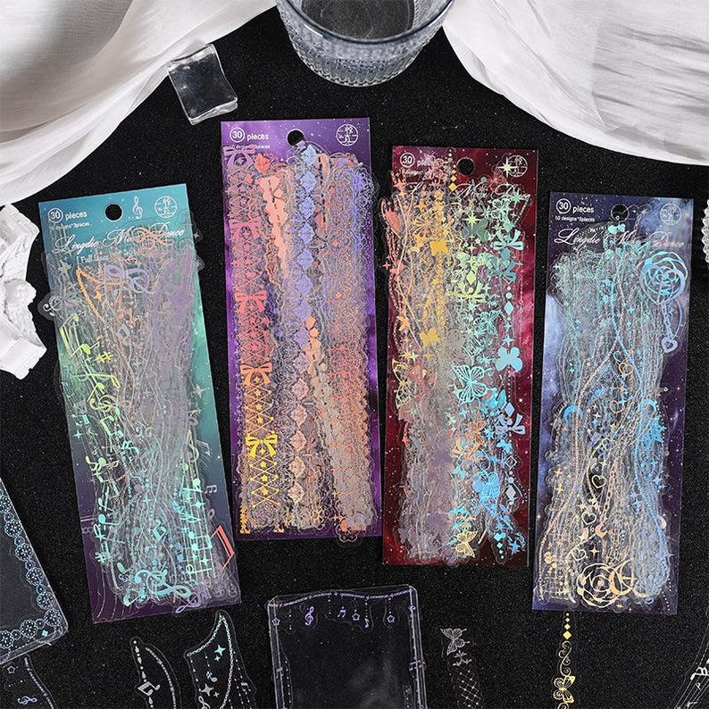 May include: Four sheets of clear, iridescent, decorative stickers with various designs. The stickers feature a variety of patterns, including musical notes, flowers, and geometric shapes. The stickers are packaged in clear plastic sleeves and labeled with the number 30 pieces.