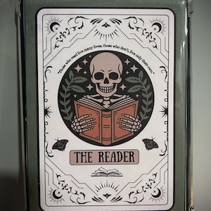 May include: A phone case with a decorative design featuring a skull reading a book. The design includes the text "Those who read live many lives; those who don't, live only their own." and "THE READER". The case has a green border.
